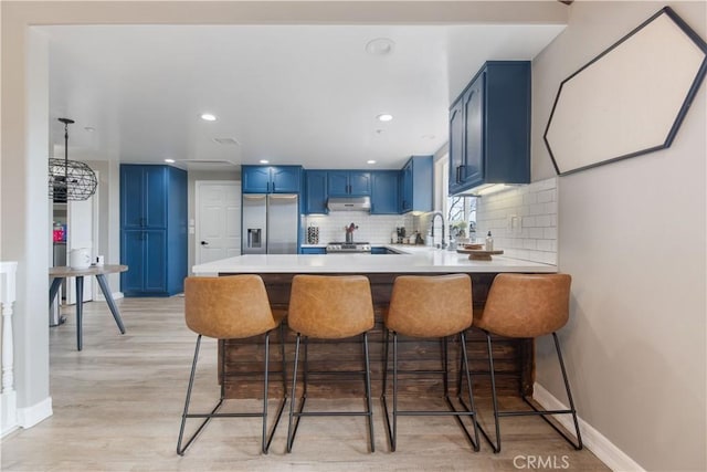 kitchen featuring stainless steel fridge, blue cabinets, a peninsula, light countertops, and under cabinet range hood