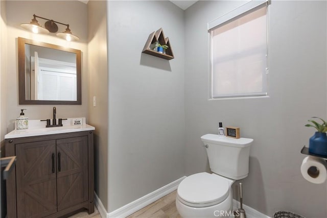 half bathroom featuring toilet, baseboards, wood finished floors, and vanity