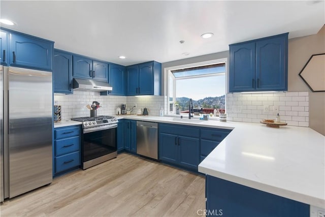 kitchen with under cabinet range hood, stainless steel appliances, light countertops, blue cabinetry, and light wood finished floors