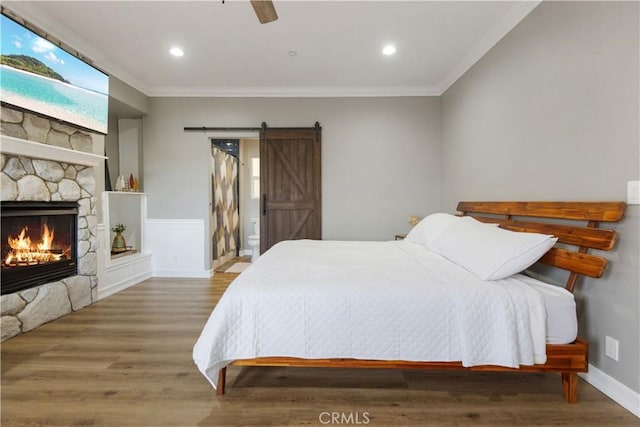 bedroom featuring a barn door, crown molding, wood finished floors, and a stone fireplace