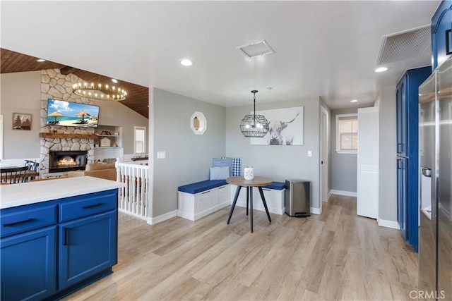 kitchen featuring a fireplace, blue cabinetry, lofted ceiling, visible vents, and light wood-style floors