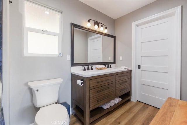 full bath with double vanity, wood finished floors, a sink, and toilet