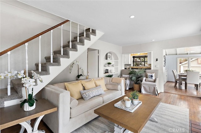 living area featuring built in shelves, stairway, wood finished floors, and recessed lighting