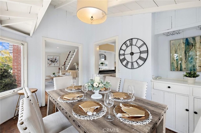 dining space featuring dark wood-style floors, vaulted ceiling with beams, and stairway