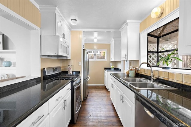 kitchen featuring dark wood finished floors, appliances with stainless steel finishes, ornamental molding, white cabinets, and a sink