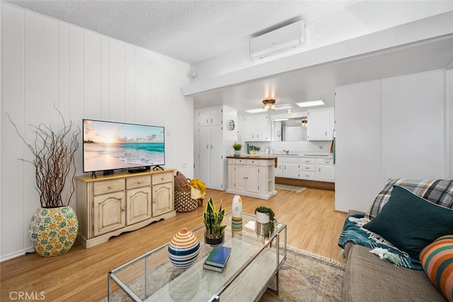 living area featuring a wall unit AC, light wood-type flooring, ceiling fan, and a textured ceiling