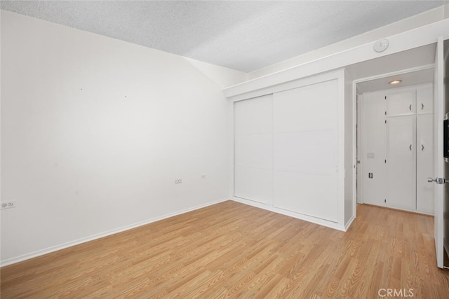 unfurnished bedroom with a closet, baseboards, a textured ceiling, and light wood finished floors