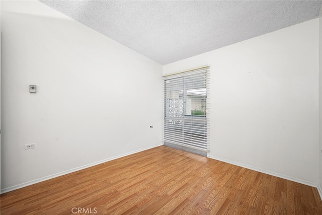 spare room with a textured ceiling, light wood-type flooring, and baseboards