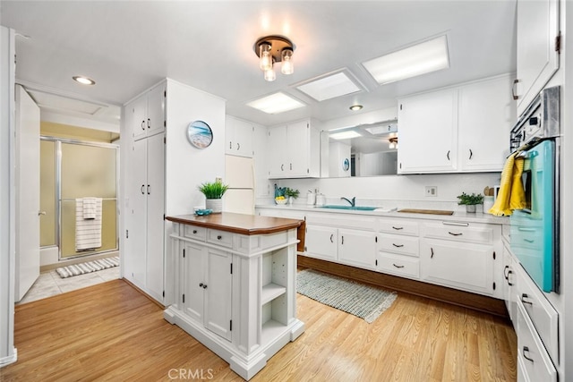 kitchen featuring light wood finished floors, open shelves, wall oven, white cabinets, and a sink