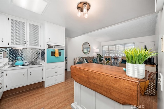 kitchen with light wood-type flooring, electric stovetop, white cabinets, and oven