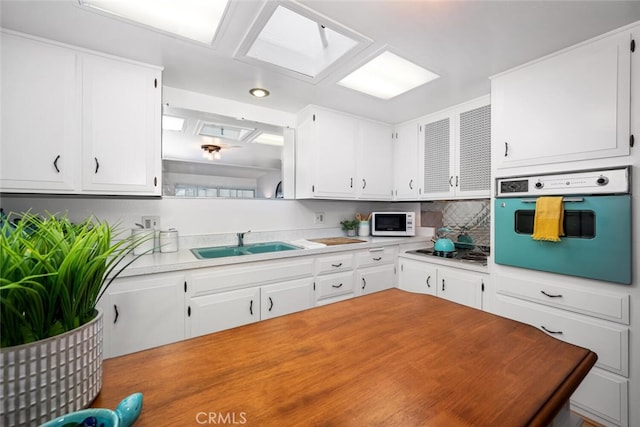 kitchen with cooktop, white microwave, oven, white cabinetry, and a sink