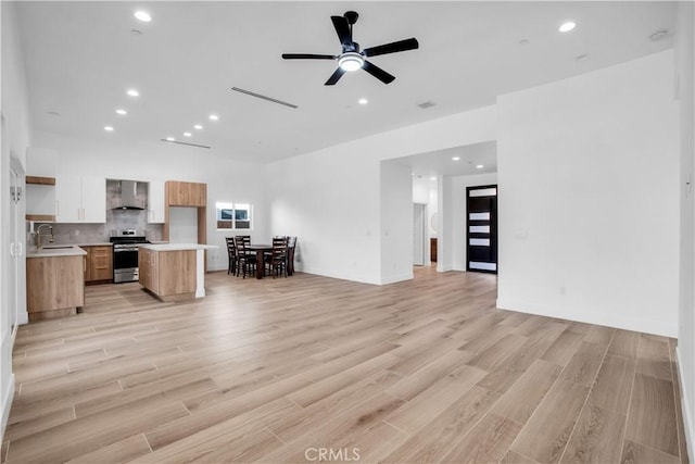 interior space with light wood-style floors, open floor plan, light countertops, stainless steel stove, and wall chimney range hood