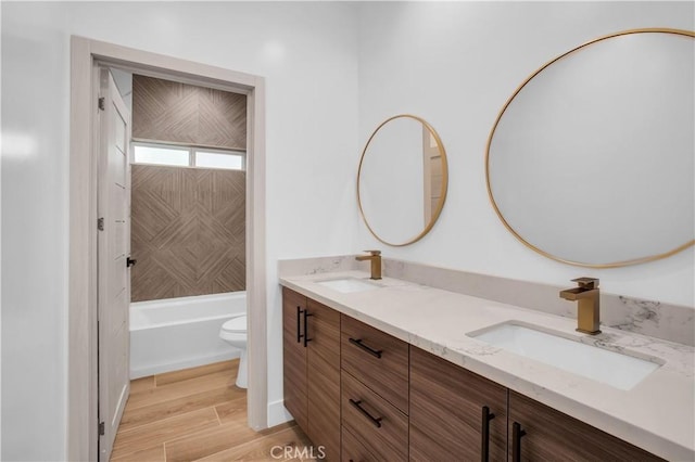 full bath featuring double vanity, toilet, a sink, and wood finished floors