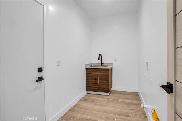 laundry room featuring light wood-type flooring, a sink, and baseboards