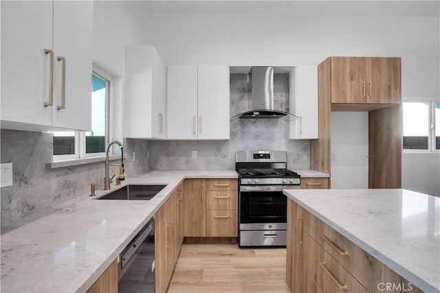 kitchen featuring a sink, white cabinetry, wall chimney range hood, appliances with stainless steel finishes, and light stone countertops