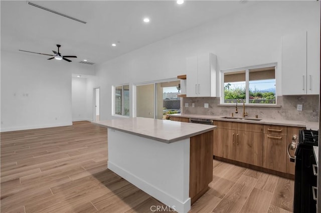 kitchen with a kitchen island, a sink, light countertops, light wood finished floors, and gas range oven