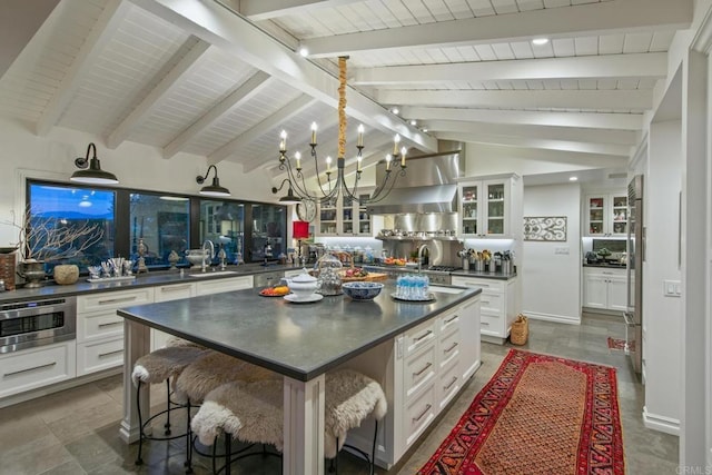 kitchen with glass insert cabinets, dark countertops, a sink, and lofted ceiling with beams