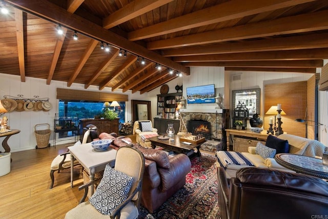 living area with lofted ceiling with beams, wooden ceiling, wood finished floors, and a stone fireplace