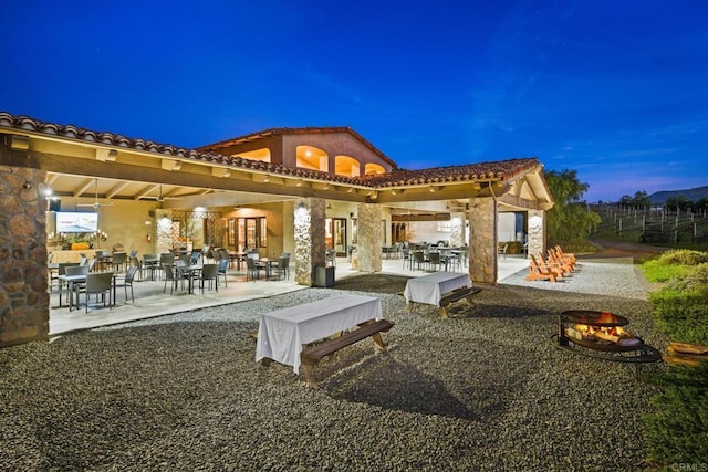 rear view of house featuring stone siding, a patio area, stucco siding, and a tiled roof