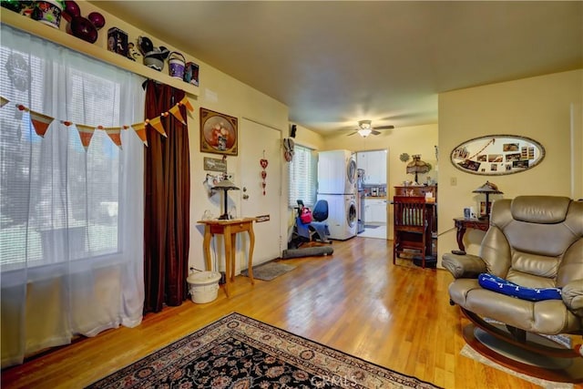 living room featuring stacked washer and clothes dryer, a ceiling fan, and wood finished floors