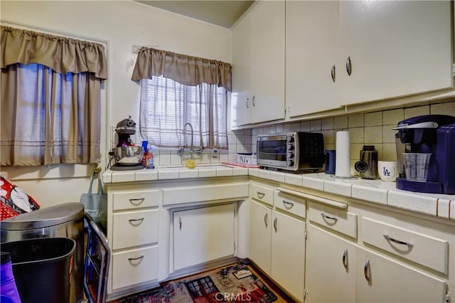 kitchen with a toaster, tile counters, white cabinets, a sink, and backsplash