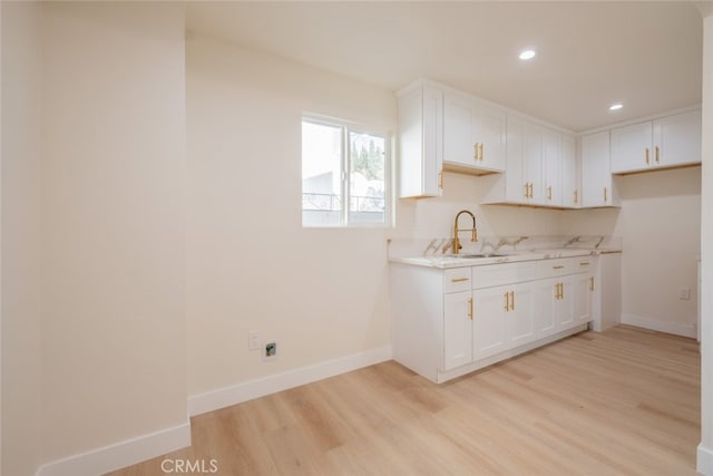 kitchen featuring light countertops, light wood-style floors, white cabinetry, a sink, and baseboards