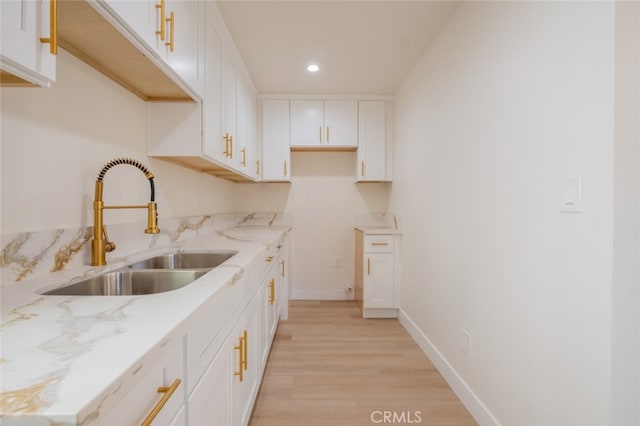 kitchen featuring light wood finished floors, baseboards, light stone countertops, white cabinetry, and a sink