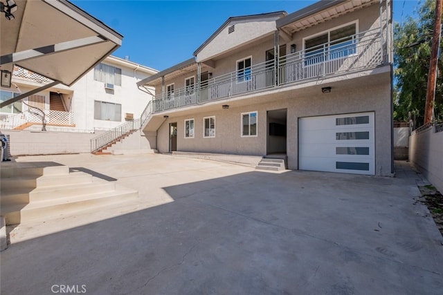 rear view of property with stairs, driveway, an attached garage, and stucco siding