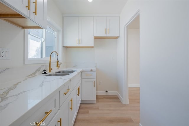 kitchen featuring light wood-style floors, a sink, white cabinetry, and light stone countertops