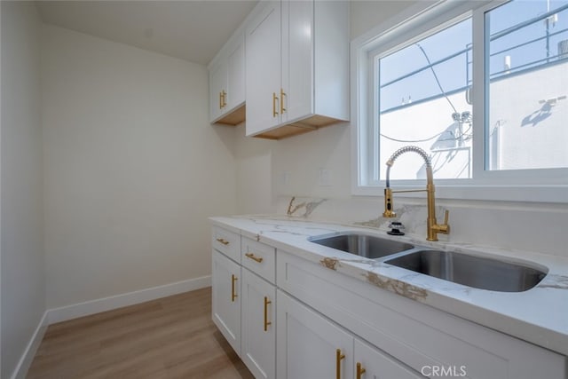 kitchen featuring light wood finished floors, baseboards, light stone counters, white cabinetry, and a sink