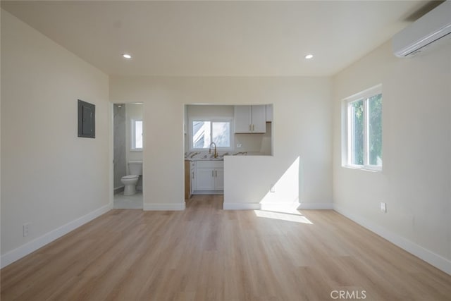 unfurnished living room featuring electric panel, plenty of natural light, baseboards, and a wall mounted AC