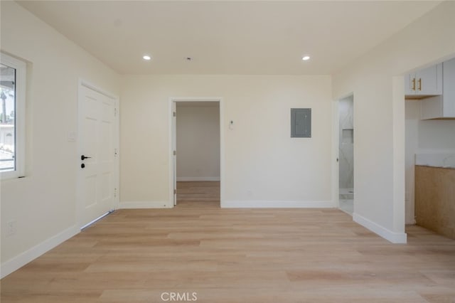 spare room featuring light wood-type flooring, electric panel, baseboards, and recessed lighting