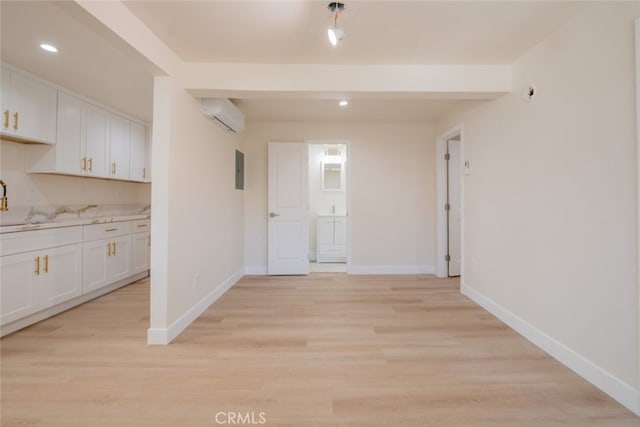 unfurnished dining area featuring light wood-type flooring, a wall mounted air conditioner, and baseboards