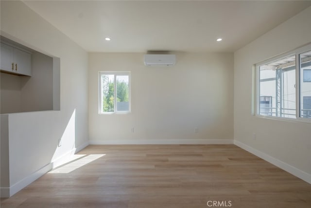 spare room featuring light wood-type flooring, a wall mounted air conditioner, baseboards, and recessed lighting