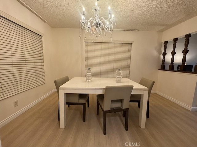 dining space with light wood-style floors, baseboards, a chandelier, and a textured ceiling