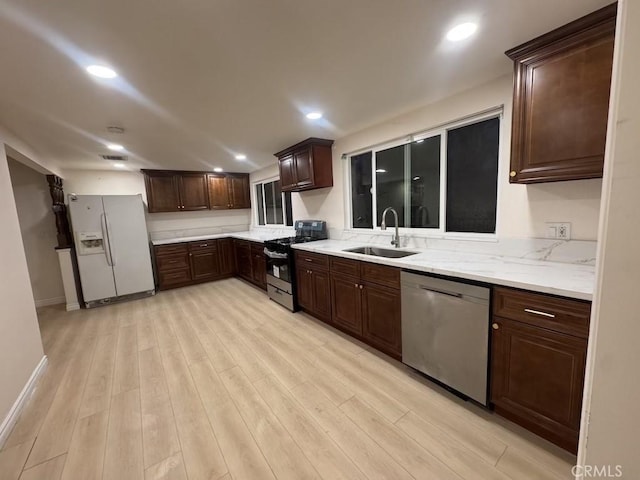 kitchen featuring black gas range oven, stainless steel dishwasher, a sink, white fridge with ice dispenser, and light wood-type flooring