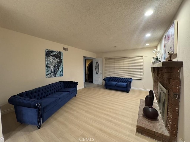 living area with a brick fireplace, baseboards, light wood-style flooring, and a textured ceiling