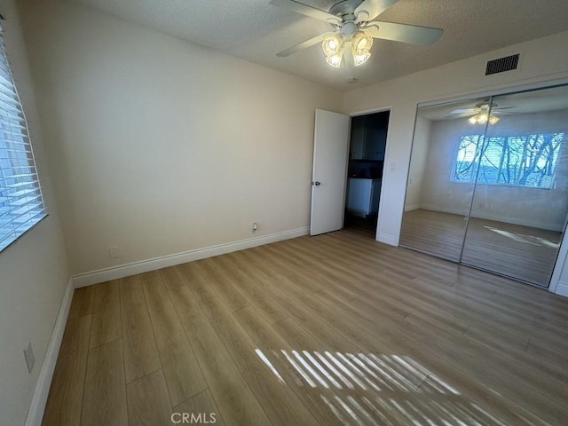 unfurnished bedroom with a textured ceiling, wood finished floors, visible vents, and baseboards