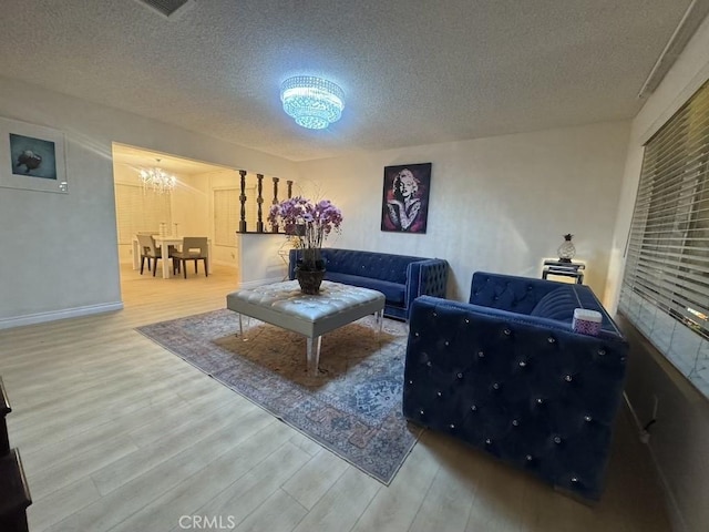 living room featuring a notable chandelier, a textured ceiling, baseboards, and wood finished floors