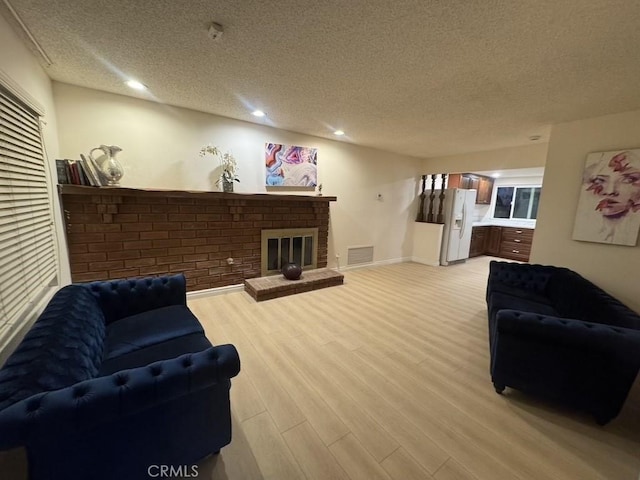 living room featuring a textured ceiling, recessed lighting, visible vents, light wood-style floors, and a brick fireplace