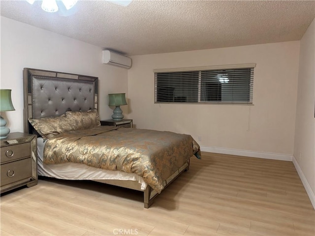 bedroom with a wall unit AC, light wood-style flooring, baseboards, and a textured ceiling