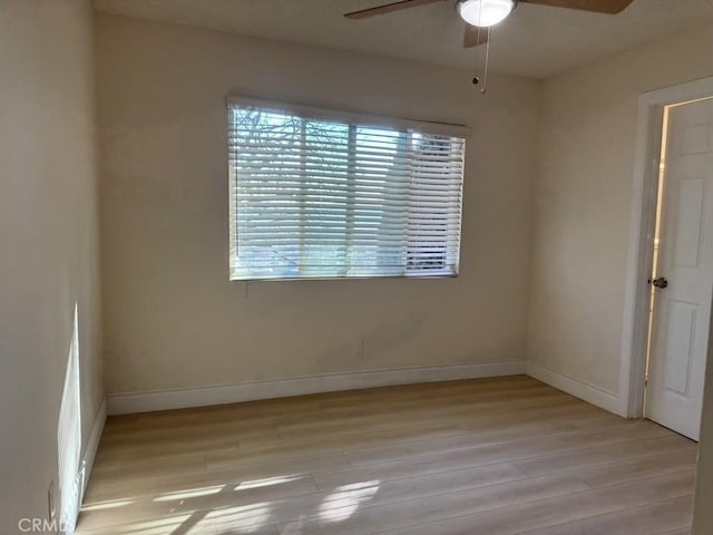 empty room with light wood-type flooring, a ceiling fan, and baseboards