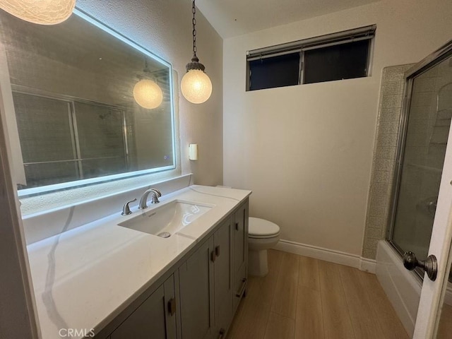 full bath with toilet, wood finished floors, vanity, baseboards, and combined bath / shower with glass door