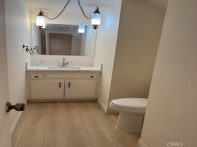 half bath featuring vanity, wood finished floors, toilet, and baseboards