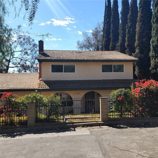 view of front of house with a fenced front yard, a tile roof, a chimney, and stucco siding