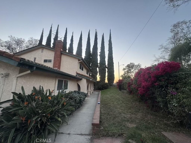 property exterior at dusk featuring a yard, a chimney, and stucco siding