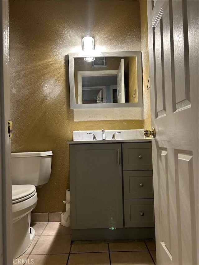 bathroom featuring a textured wall, toilet, vanity, baseboards, and tile patterned floors