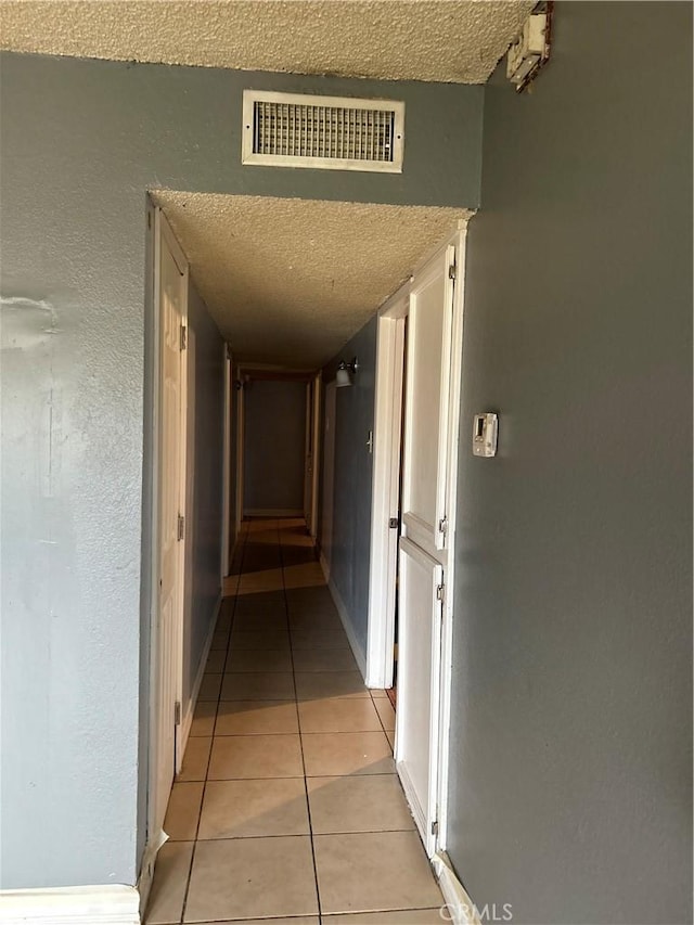 hallway featuring light tile patterned floors, visible vents, and a textured ceiling