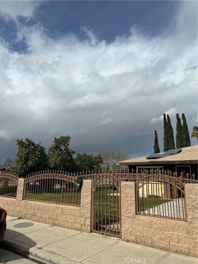 view of gate with a fenced front yard and roof mounted solar panels