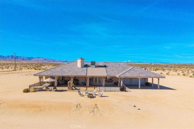 rear view of house featuring a chimney, dirt driveway, a mountain view, and view of desert